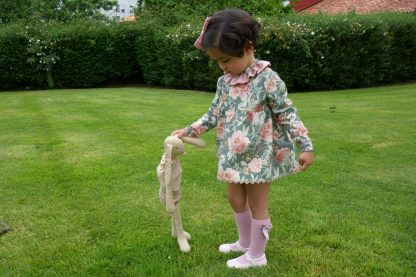 Niña vestida con un conjunto verde estampado flores en un jardin jugado con muñeca. Modelo Garden.