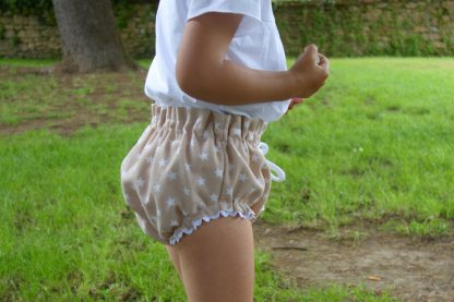 Busto de niña con culotte estrellas beige en un prado.