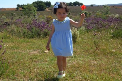 Niña en el campo que lleva puesto vestido plumeti azul con detalles en amarillo.