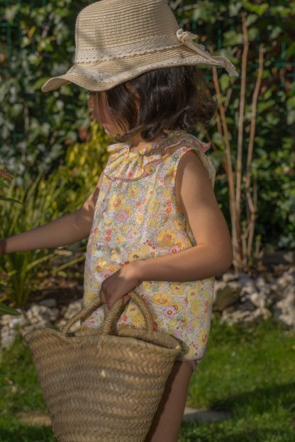 Niña en jardín vestida con blusa sin mangas de flores liberty amarillo, rosa y verde.