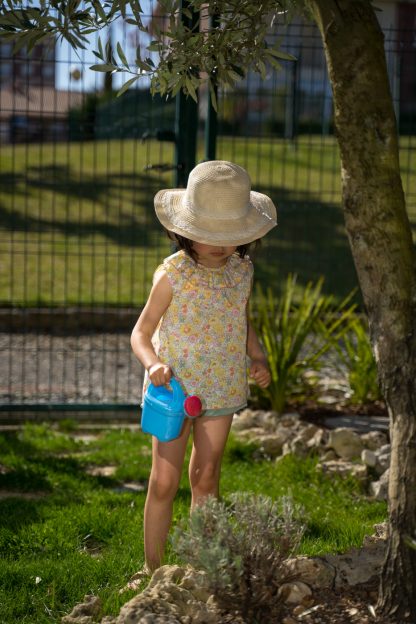 Niña en jardín vestida con blusa sin mangas de flores liberty amarillo, rosa y verde y bombacho verde a juego.